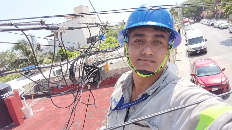 Jorge in a hard hat next to a fiber distribution box on a rooftop